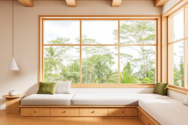 istock Cozy minimalist interior with large wooden-framed windows and built-in seating overlooking lush tropical greenery in daylight. 3D Rendering 2228289227