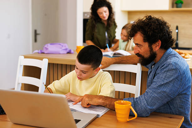 istock Father helping son with homework in kitchen while mother supervises daughter 2228289582