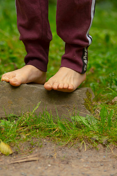 istock A childs bare feet gently stand on a stone in the green grass 2228290003