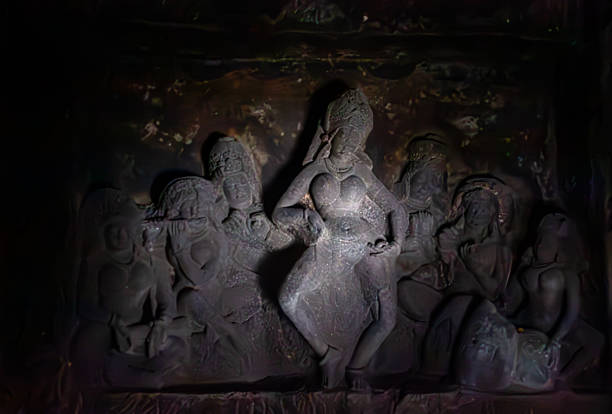 Intricately carved ancient stone sculptures of figures adorn a dimly lit wall within the Aurangabad Caves. The worn details and textures of the rock highlight the historical artistry and cultural significance of these religious or mythological depictions, creating a solemn atmosphere.