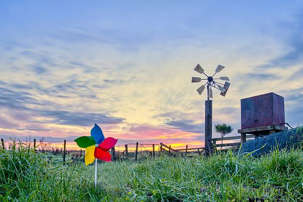 Farm wind water pump looking a bit run down with it's water tower next to it. Also a wonderful sunrise sky in the background.