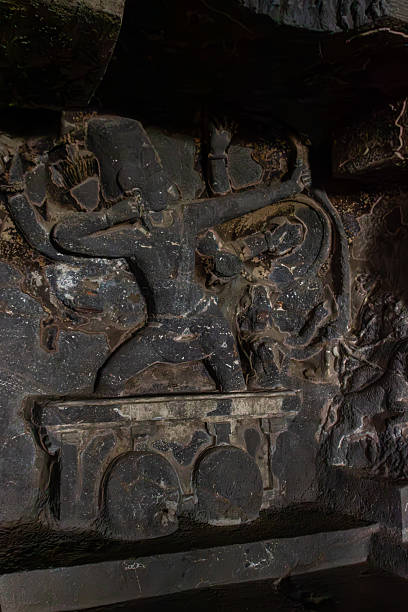 A compelling ancient stone carving depicts Lord Shiva as Tripurantaka, the destroyer of Tripura, in a dynamic warrior pose, holding a weapon, intricately carved into a deep, dimly lit niche within the rock-cut caves of Ellora, showcasing the detailed artistry and mythological narrative of divine power.