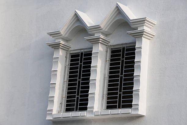 Two windows with ornate, decorative frames and security grilles in front of the windowpanes with traditional architecture