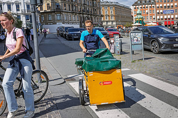 Copenhagen, Denmark, April 29, 2025:  A mail carrier in a blue PostNord uniform rides a yellow electric cargo bike from the former Post Danmark. In the Danish capital, much of the goods transport is done by electric bikes rather than cars.