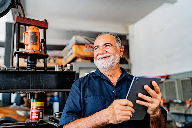 Senior mechanic man contemplating while using digital tablet at auto repair shop