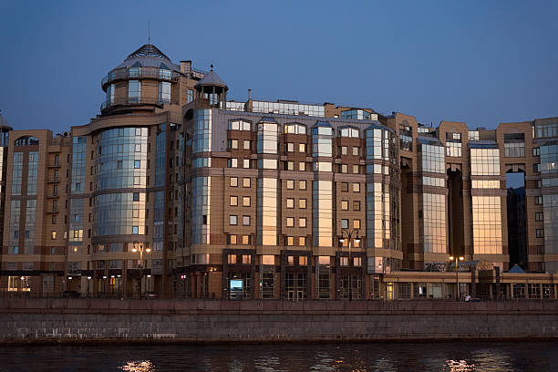 A stunning modern building featuring a glass facade that cleverly reflects the evening sky over the tranquil river