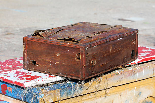 A battered, antique-style wooden box with warped panels, peeling surfaces, and visible distress marks, placed outdoors on colorful, paint-chipped boards
