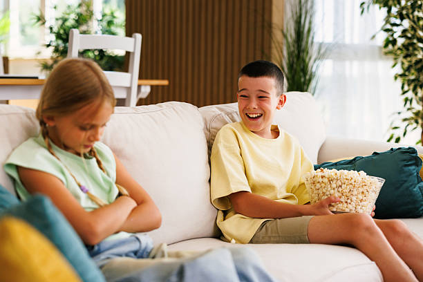 istock Boy laughing and eating popcorn while sister is angry on sofa 2228309577