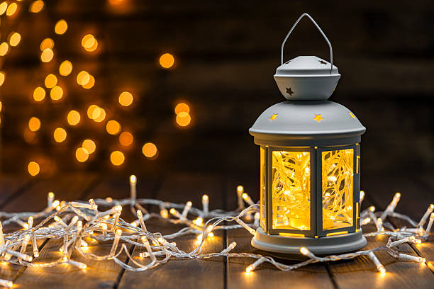 Illuminated Christmas string lights in a lantern on wood paneling. Holidays or December background or Holiday spirit. Copy space