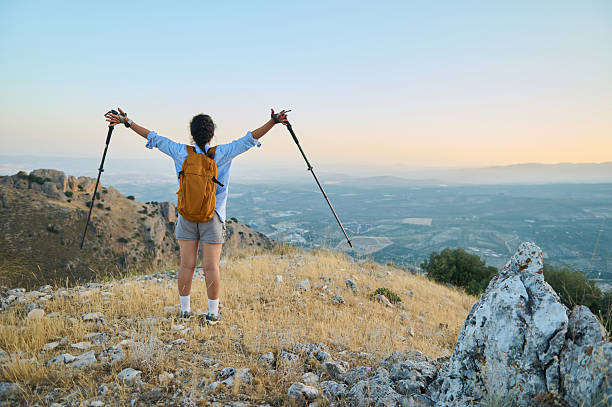 istock Hiker on Mountain Summit at Sunrise with Raised Trekking Poles and Backpack 2228315826