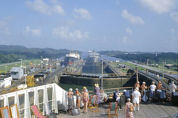 Panama Canal, Panama, 1982. Vacationers on a cruise ship look out from the bow of the ship at a large lock system of the Panama Canal. Also: merchant ships.