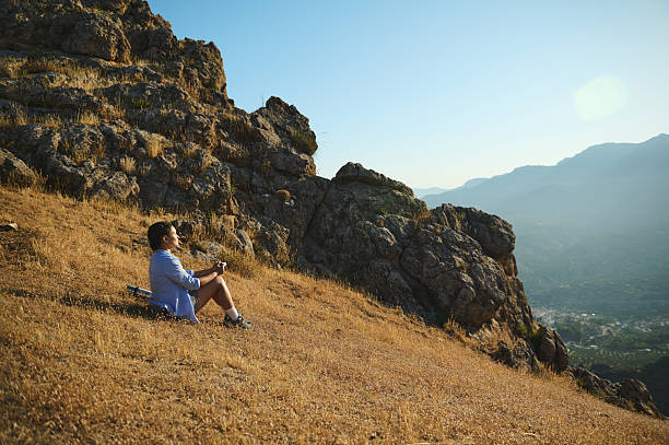 istock Man Relaxing on a Hillside with Scenic Mountain Views at Sunset 2228318603
