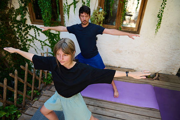 istock Two People Practicing Yoga Outdoors on a Wooden Patio Surrounded by Greenery 2228324535
