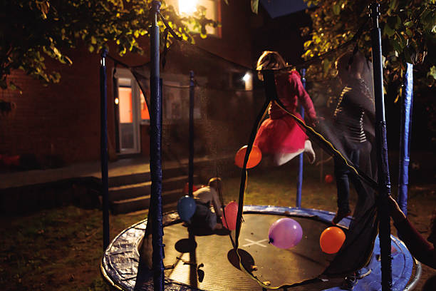 Children having fun playing at an outdoor backyard birthday party, jumping in trampoline and throwing balloons