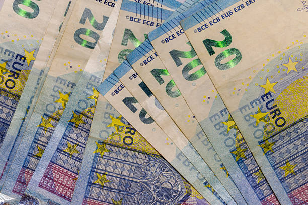 Close-up of several 20 Euro banknotes, fanned out to display their features. Predominant colors are light beige, blue, yellow and slight pink details.
