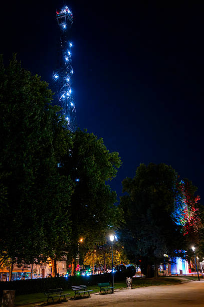Night view of a lit tower in a city park with benches and trees, capturing urban nightlife ambiance.