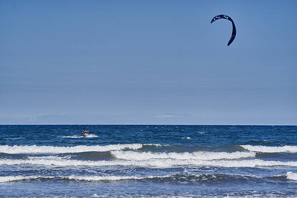 Spain, Canary Islands, Tenerife, Playa del Médano 05 June 2025 - Young woman kitesurfing on open ocean under blue canopy and clear sky