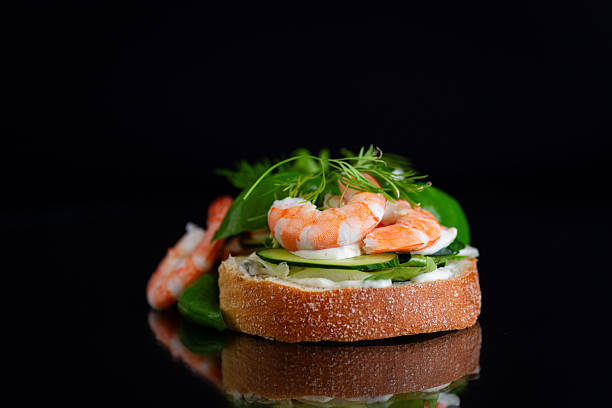 istock Small canapes with shrimps, salad and cucumbers on a black background 2228340087