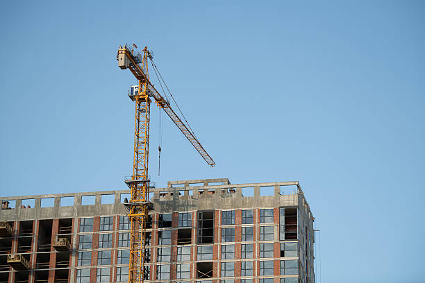 istock A towering construction crane is actively lifting materials at a building site in an urban area under blue skies. The structure is in mid-construction, showcasing progress 2228345143