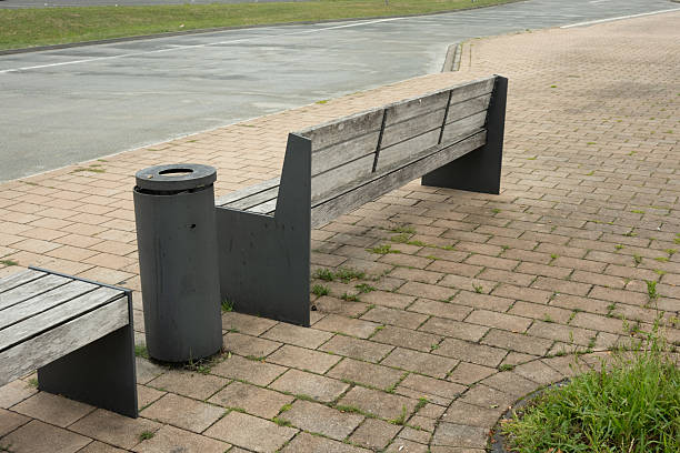 istock Empty bench with trash can on brick sidewalk near road 2228351786