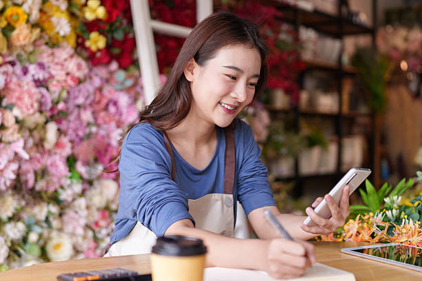istock Asian Florist Owner Managing Artificial Flower Shop Orders Online and Writing Notes for Customer Engagement 2228352977