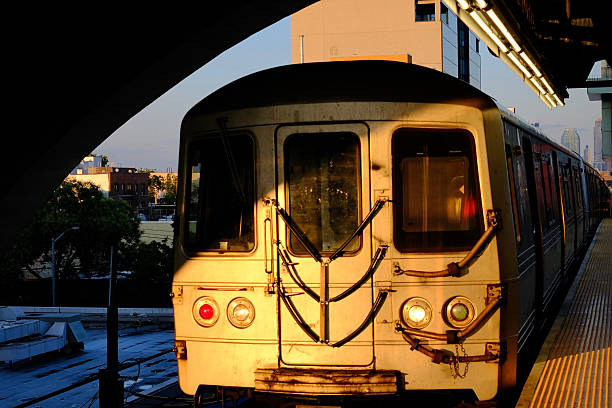 A subway train parked in an elevated station is illuminated by the golden morning sun, with the station’s arch directly above it.