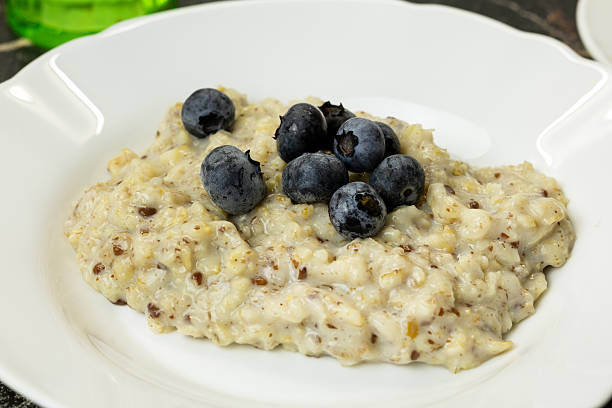 A bowl of oatmeal topped with fresh blueberries. The dish is creamy and served on a white plate. The background is softly blurred.