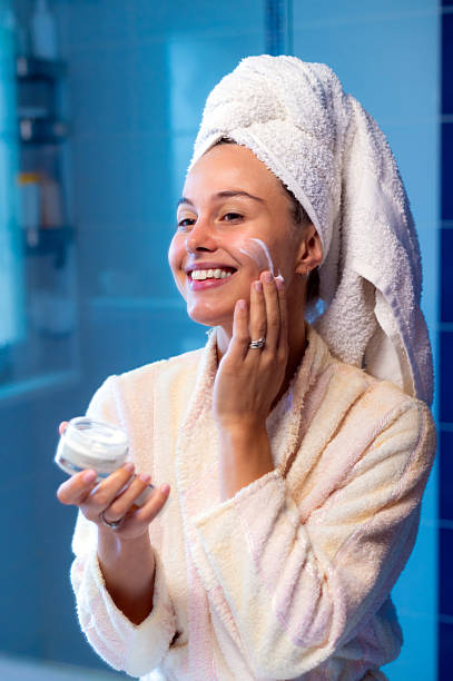 istock Smiling woman putting moisturizer cream on her face after showering 2228384817
