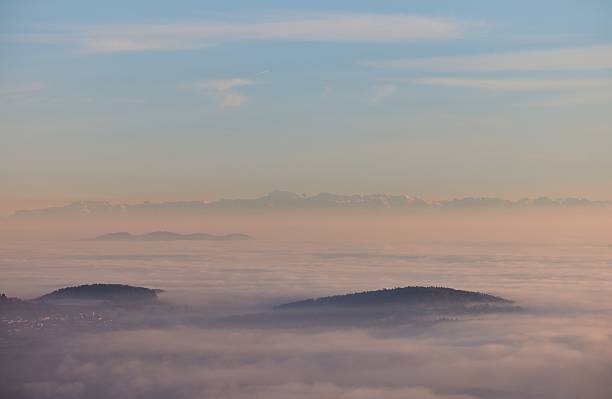 A serene view of misty hills and distant mountains under a pastel sky, creating a tranquil landscape scene.