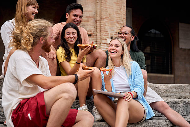 istock Happy friends eating pizza outdoors, sitting on ancient stone steps 2228387218