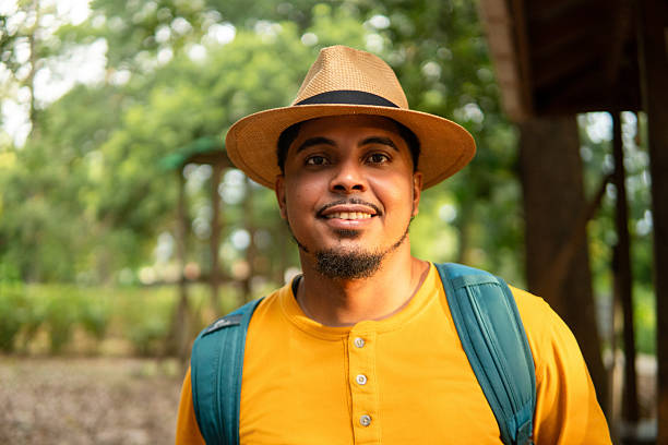 Smiling hiker wearing straw hat and backpack standing in verdant forest, experiencing tranquility and connecting with natural surroundings for personal wellness and stress relief