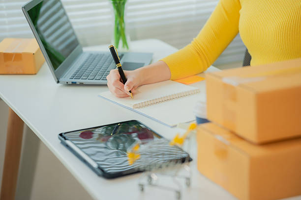 istock SME supply chain concept, procurement, Asian female entrepreneur taking notes while working on laptop, customer is managing orders in small business store. 2228398458