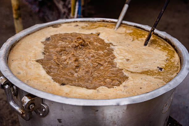 Large metal pot boiling a thick brown stew outdoors with foam and bubbles.