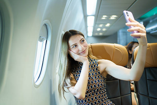 A Western female passenger is seated by the airplane window, enjoying the scenic view outside while flying. She is relaxed and immersed in the experience of air travel and sightseeing.