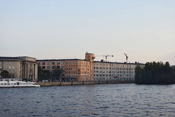 A serene riverside scene featuring modern buildings and construction activities against a sunset sky.
