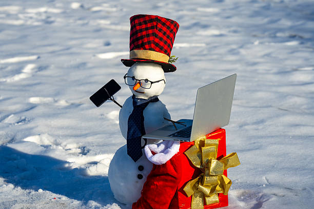 istock Snowman making a phone call and using laptop. Funny snowman talking on mobile in snow. Winter online greetings. Snowman businessman outside. Winter internet connection. Online snowman. 2228410024