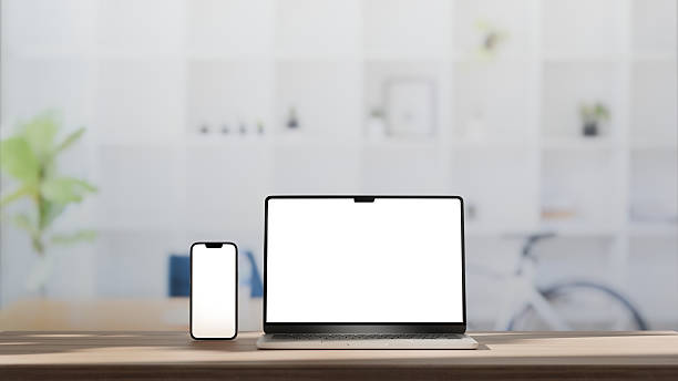 Laptop and smartphone with blank white screens on a wooden desk in a bright office stock photo