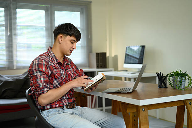 istock Young man writing in notebook while sitting at desk with laptop in home office 2228412181