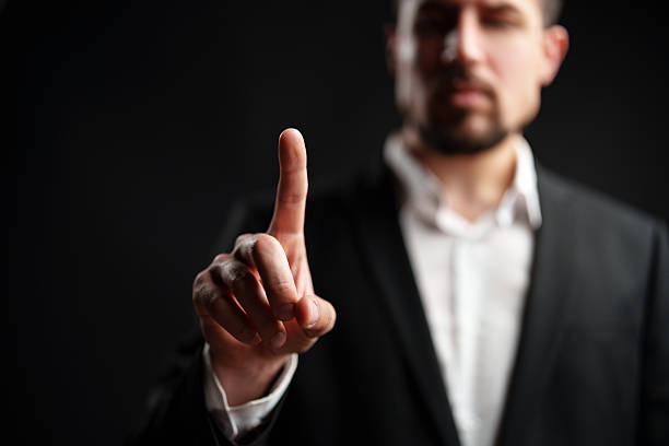 istock Man in a suit holds one finger up against a dark background to convey a message or emphasize a point during a serious discussion 2228422556