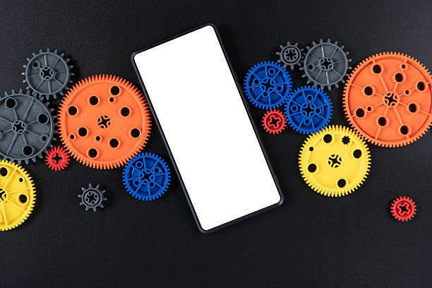 Top view of colorful plastic gears around blank smartphone screen on black background. Concept for mobile technology, creativity, innovation, STEM education, and digital engineering tools.
