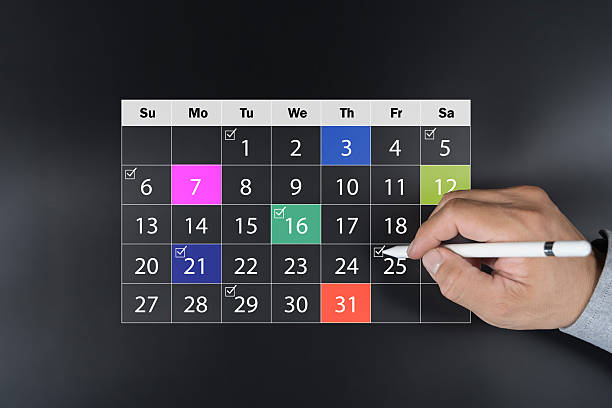 Close-up of hand using white pen to mark dates on a colorful calendar. Concept for schedule planning, time management, deadline reminder, event tracking, and productivity in daily or monthly routine.