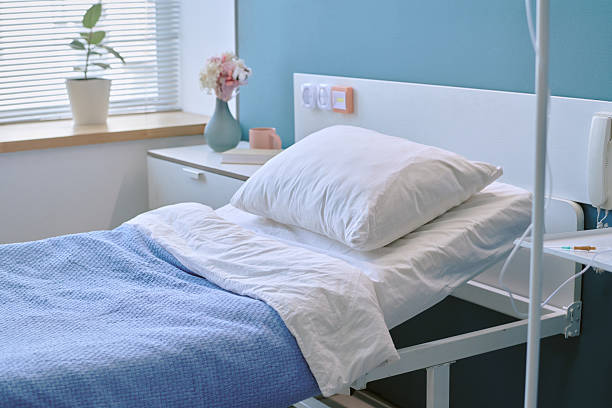 istock Empty Hospital Bed with Pillow and Blue Blanket in Sunlit Patient Room 2228426229
