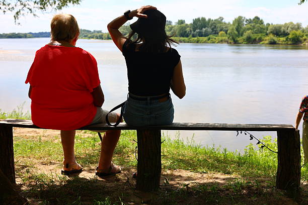 Sandomierz, Poland - July 24, 2025: Two people sitting on a bench overlooking a river on a sunny day.