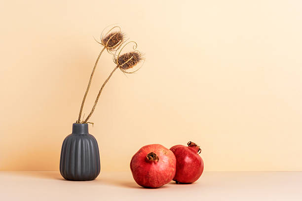 istock Dry thistle in a grey vase and two ripe pomegranates on a neutral beige background. Minimalistic autumn still life, copy space 2228437908