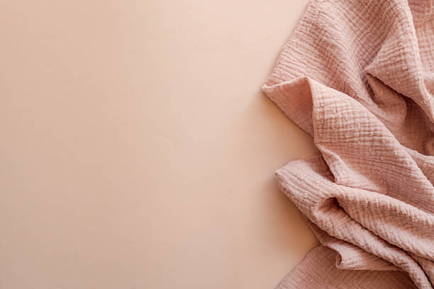 istock Textured pink muslin fabric softly draped on a pastel beige background. Delicate and minimal setup ideal for baby product design, branding mockups, or fabric pattern showcasing 2228438175