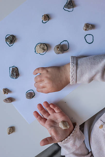 istock Toddler engaging in a rock sorting and matching activity, placing natural stones on drawn outlines. Montessori-inspired learning for sensory development and hand-eye coordination 2228438580
