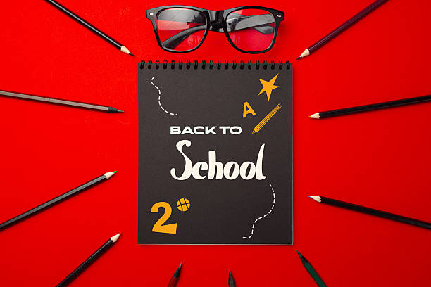istock Creative back to school display with notebook, glasses, and colorful pencils on red background during preparation for new academic year 2228438877