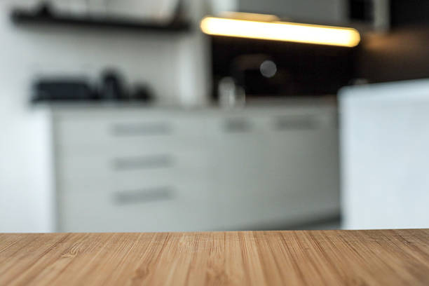 istock Wooden tabletop with blurred modern kitchen interior in the background. Soft lighting from under-cabinet LED strip highlights the minimalist black and white cabinetry 2228439228
