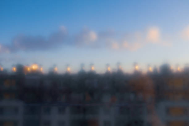 Blurry image of a city skyline with a cloudy sky. The buildings are tall and the lights are on, creating a sense of a bustling urban environment