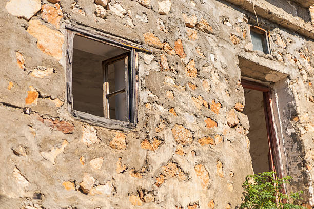 istock Sunlight highlights an abandoned building's weathered stone wall adorned with two window openings. The construction reflects nature's wear and time's passage in a serene rural landscape 2228451219